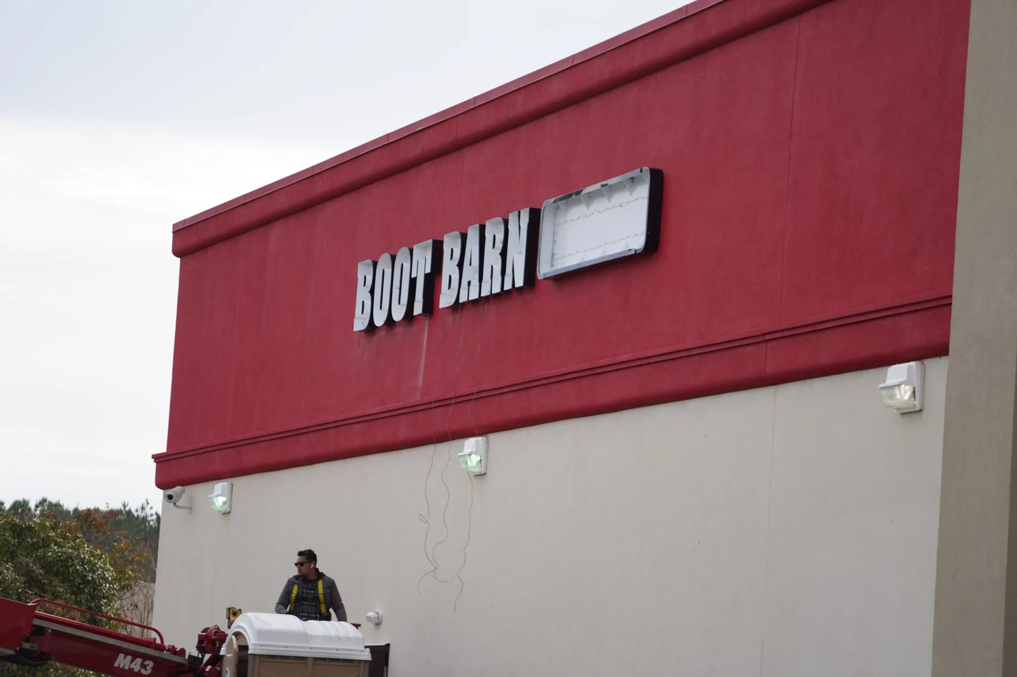 Worker in an aerial lift below Boot Barn wall lettering with an open sign cabinet