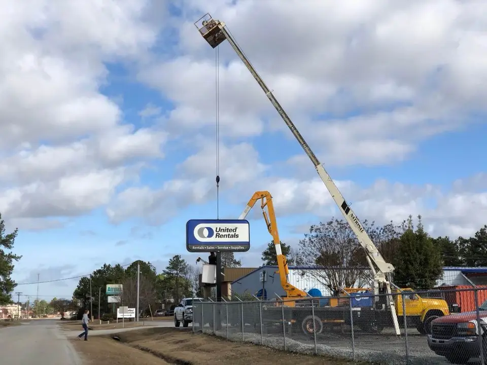 Crane and aerial lift beside a United Rentals pole sign